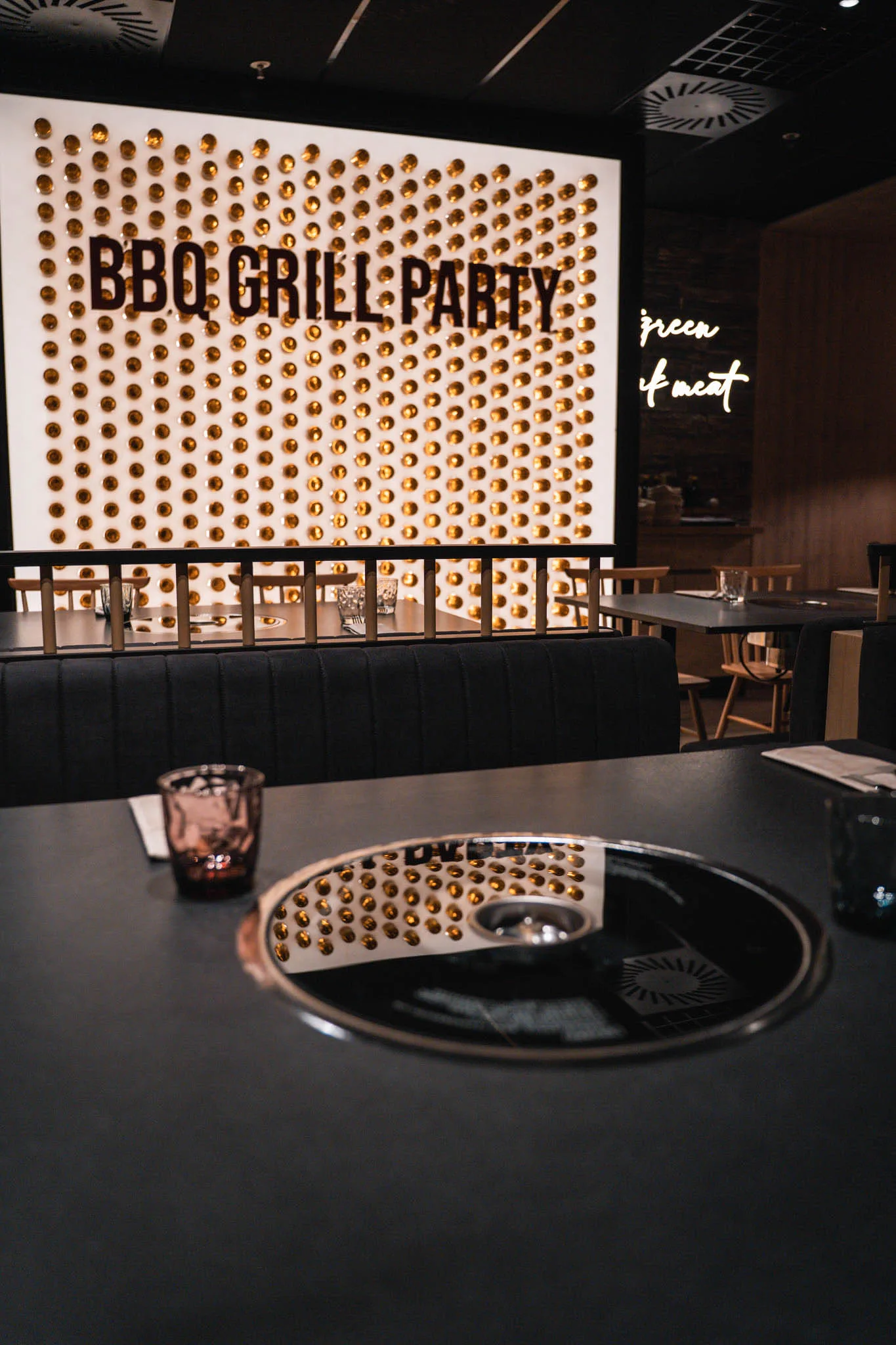 Parete di bicchieri dorati con la scritta BBQ Grill Party, davanti il tavolo con la griglia