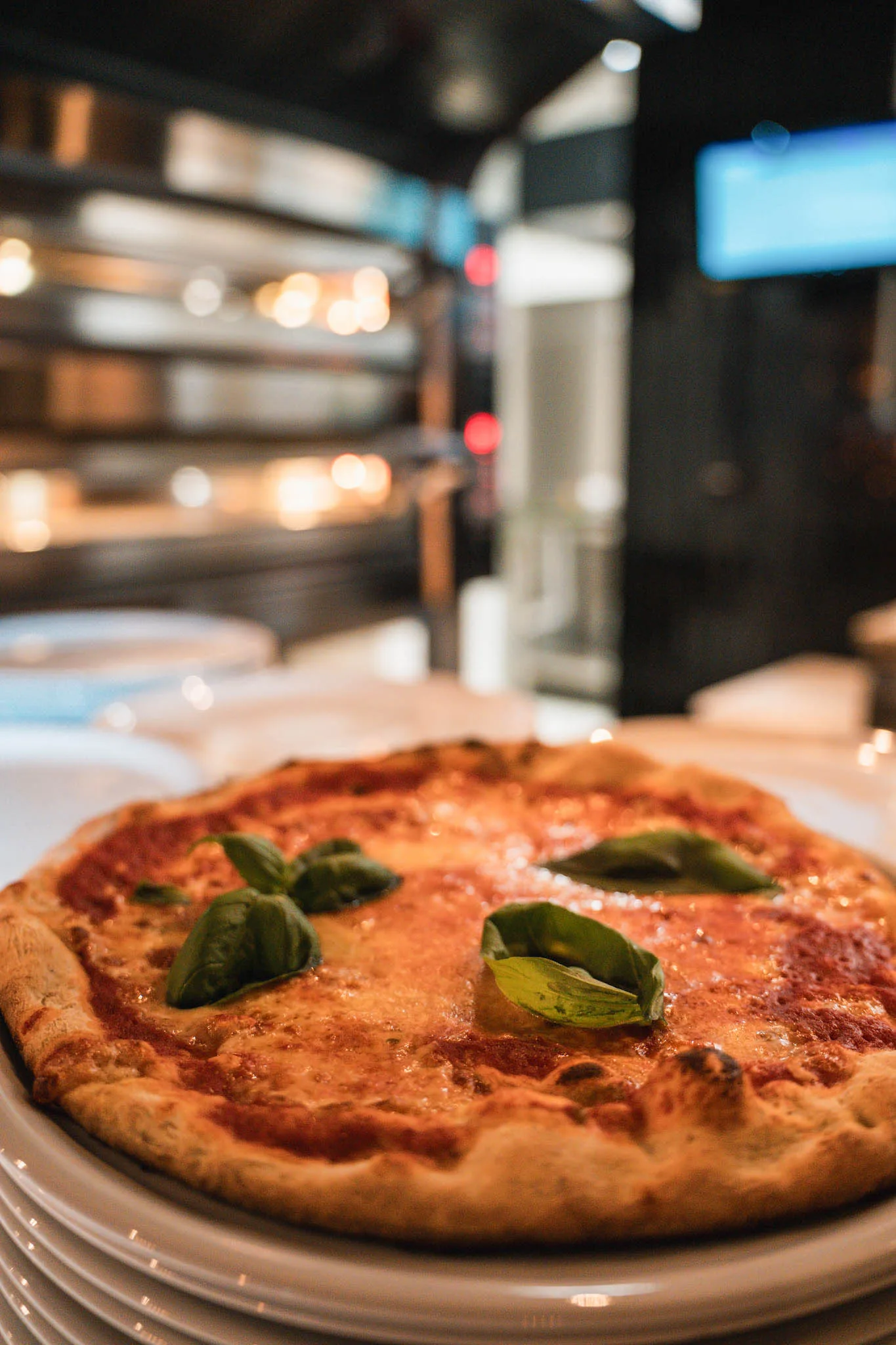 Pizza Margherita mit Basilikum, dahinter der Ofen
