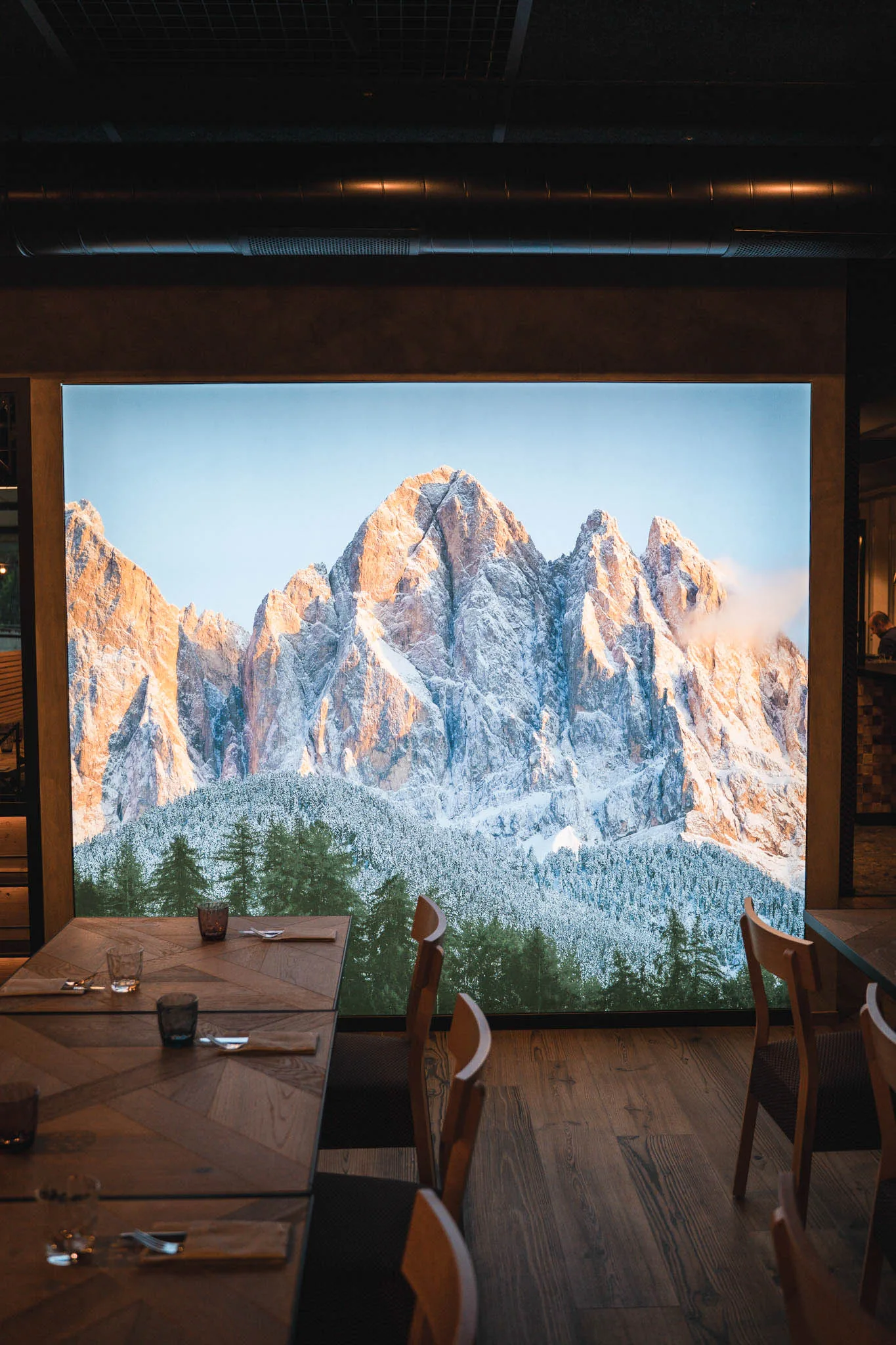 Gedeckte Holztische vor einer wandfüllenden Dolomiten-Aufnahme