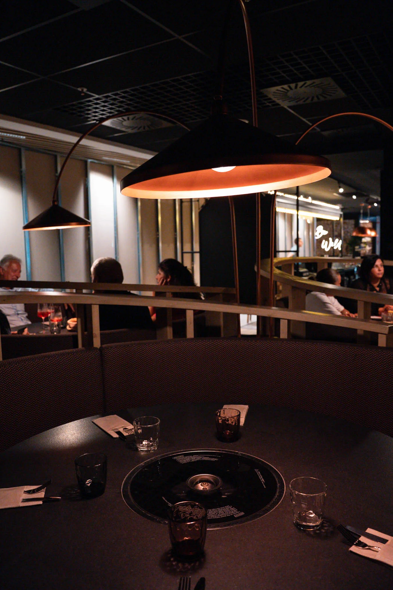Grill im Tisch unter der Kupferlampe, dahinter die Runde im BBQ-Raum
